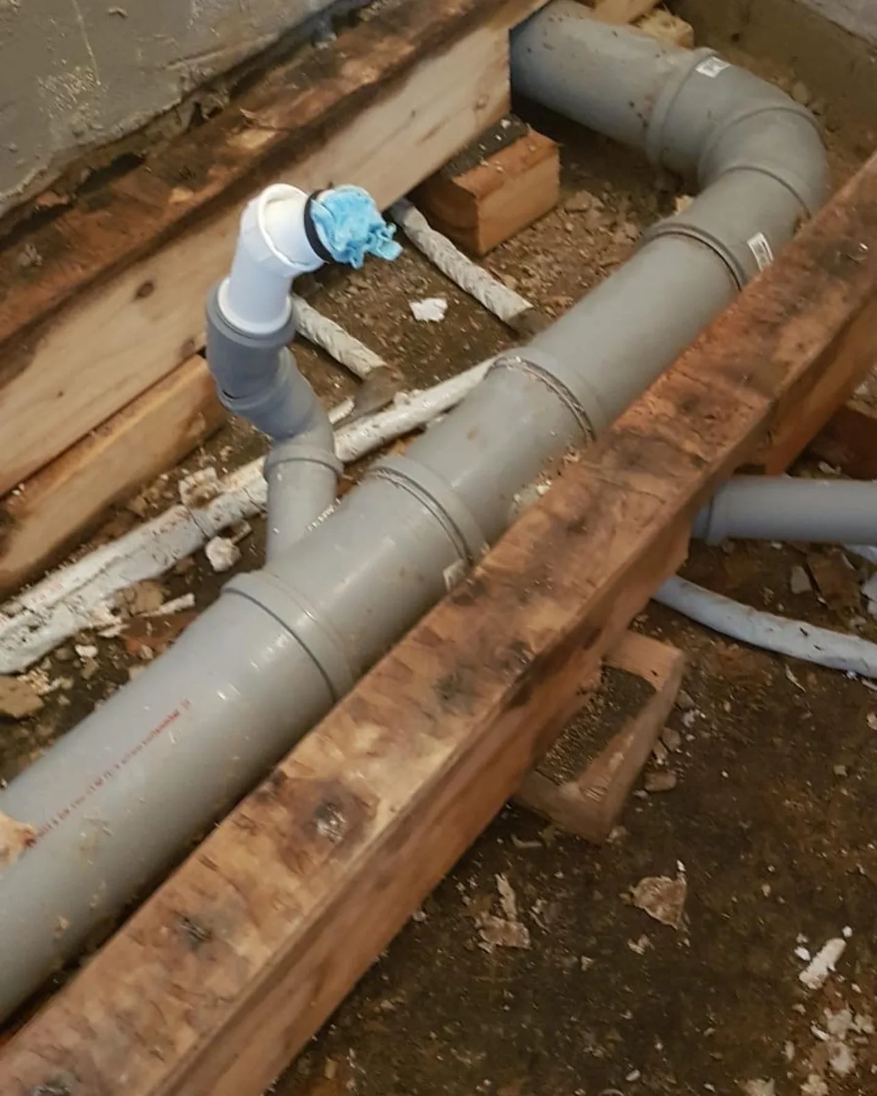 Badezimmer im Rohbauzustand: freigelegte Abflussrohre, offener Bodenaufbau, Bauschutt