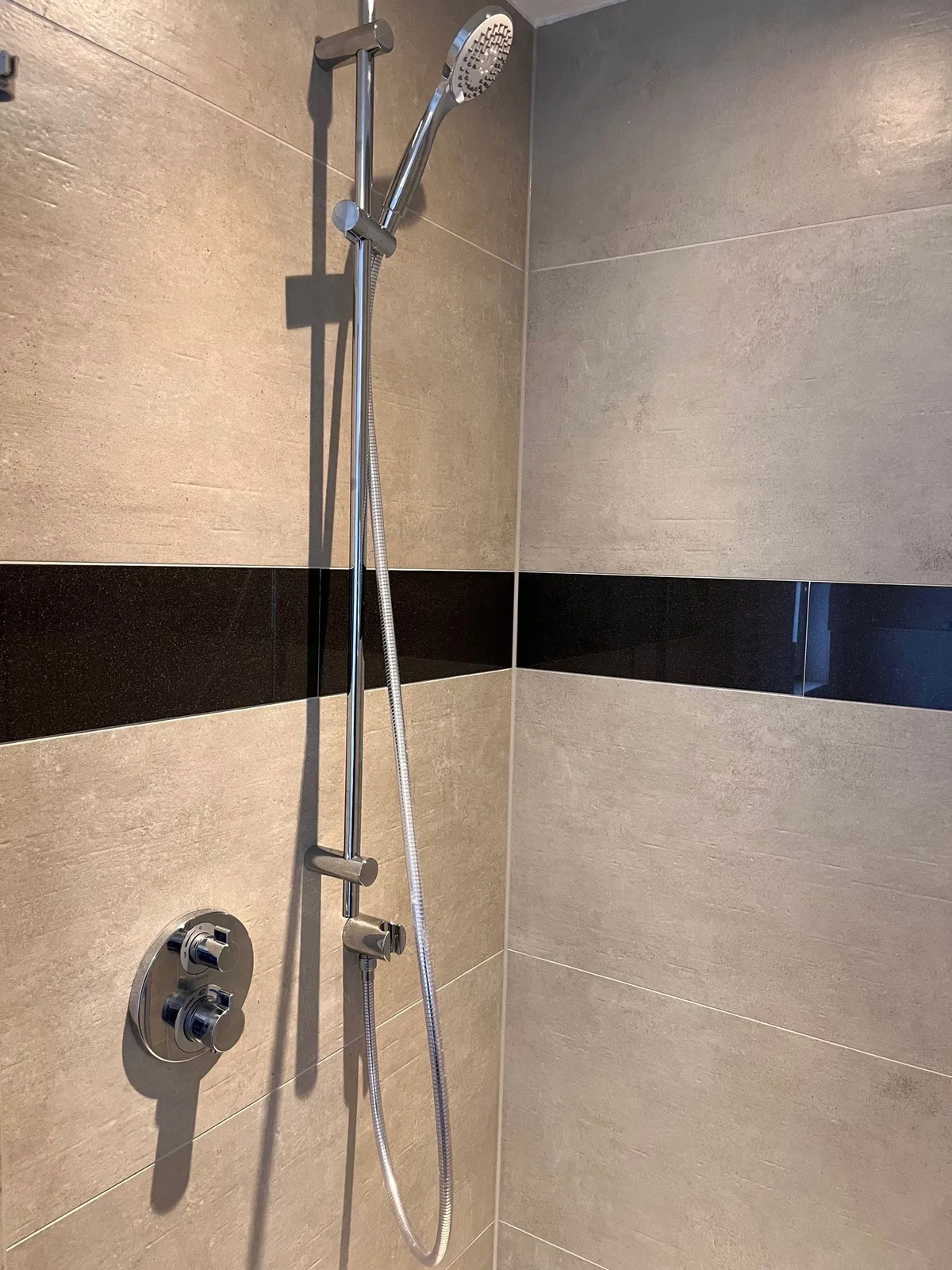 Fertige Dusche mit Armatur und dunklem Fliesenband