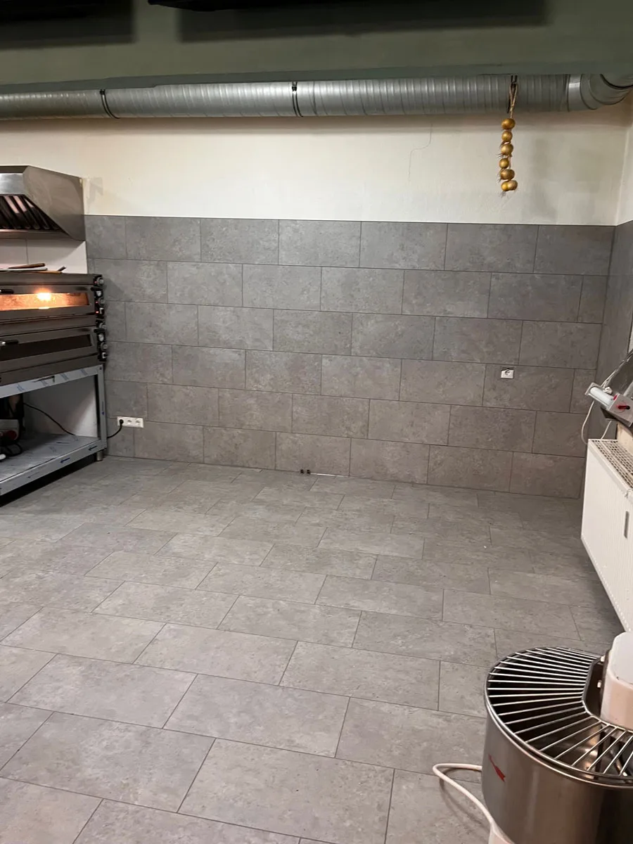Sanierte Gewerbeküche mit gefliesten Wänden, Backofen und Teigmaschine